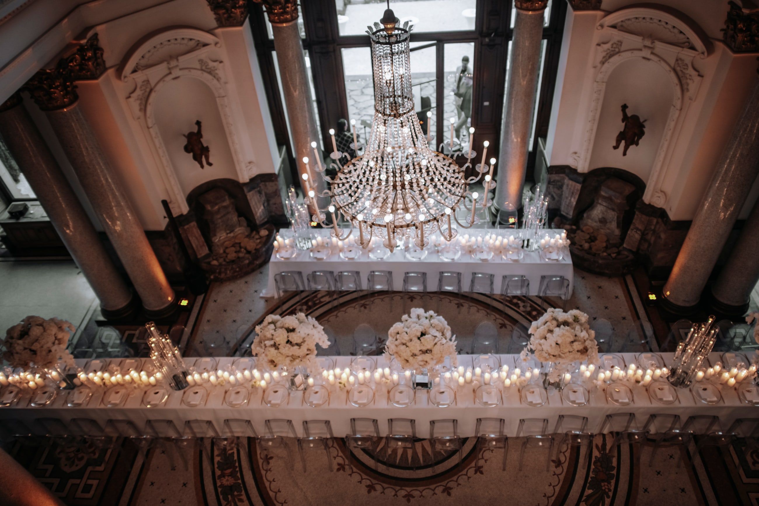 Der Kuppelsaal der Stella Rheni von oben, lange weiße Hochzeitstafeln mit Kerzen und weißen Blumen unter einem großen Kristallleuchter