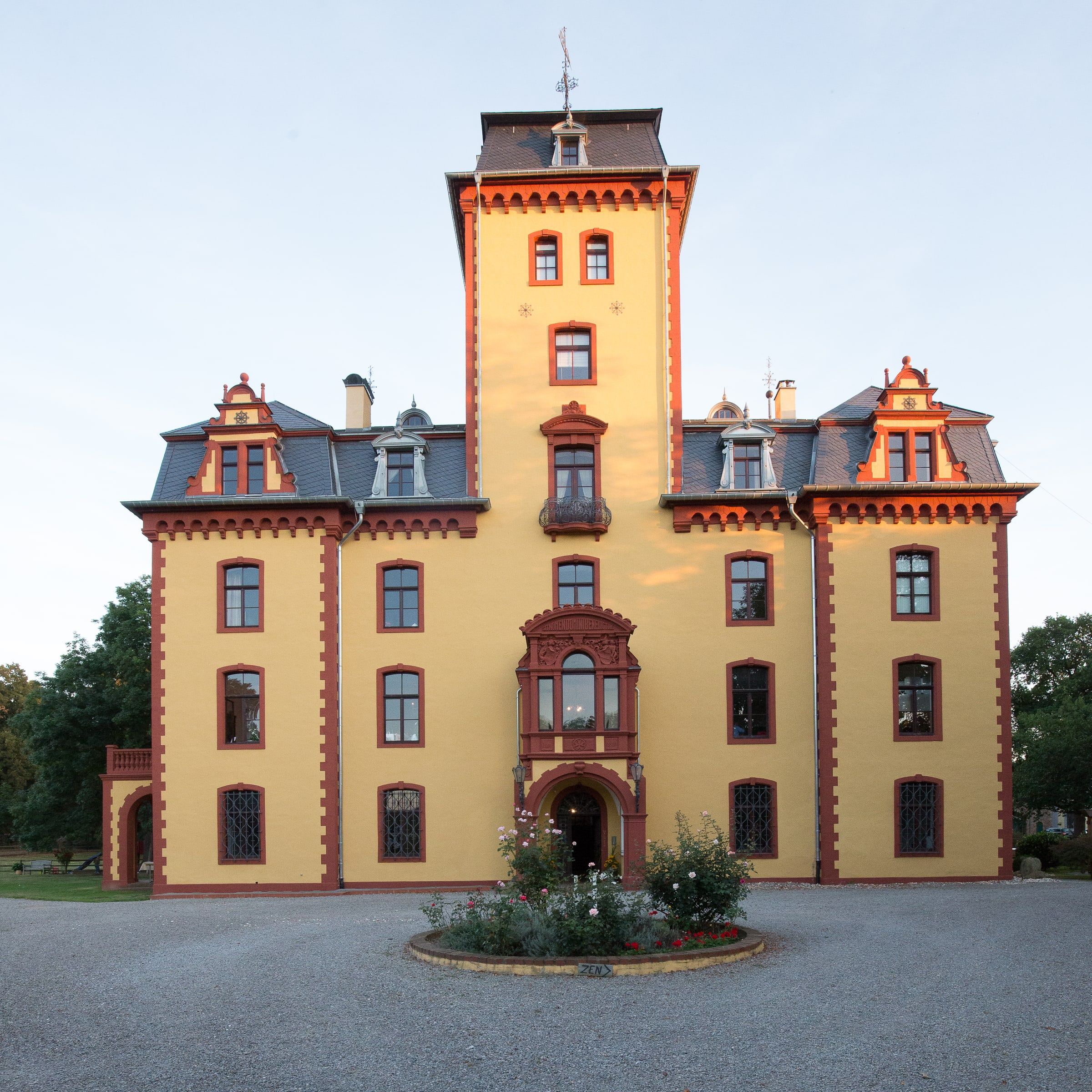 Die gelbe Fassade von Schloss Wachendorf mit Mittelturm, Erker und verzierten Giebeln, frontal vor hellem Himmel